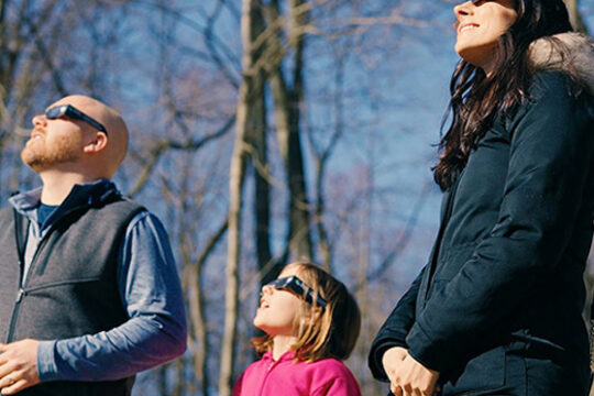 a family wearing eclipse glasses while watching a solar eclipse