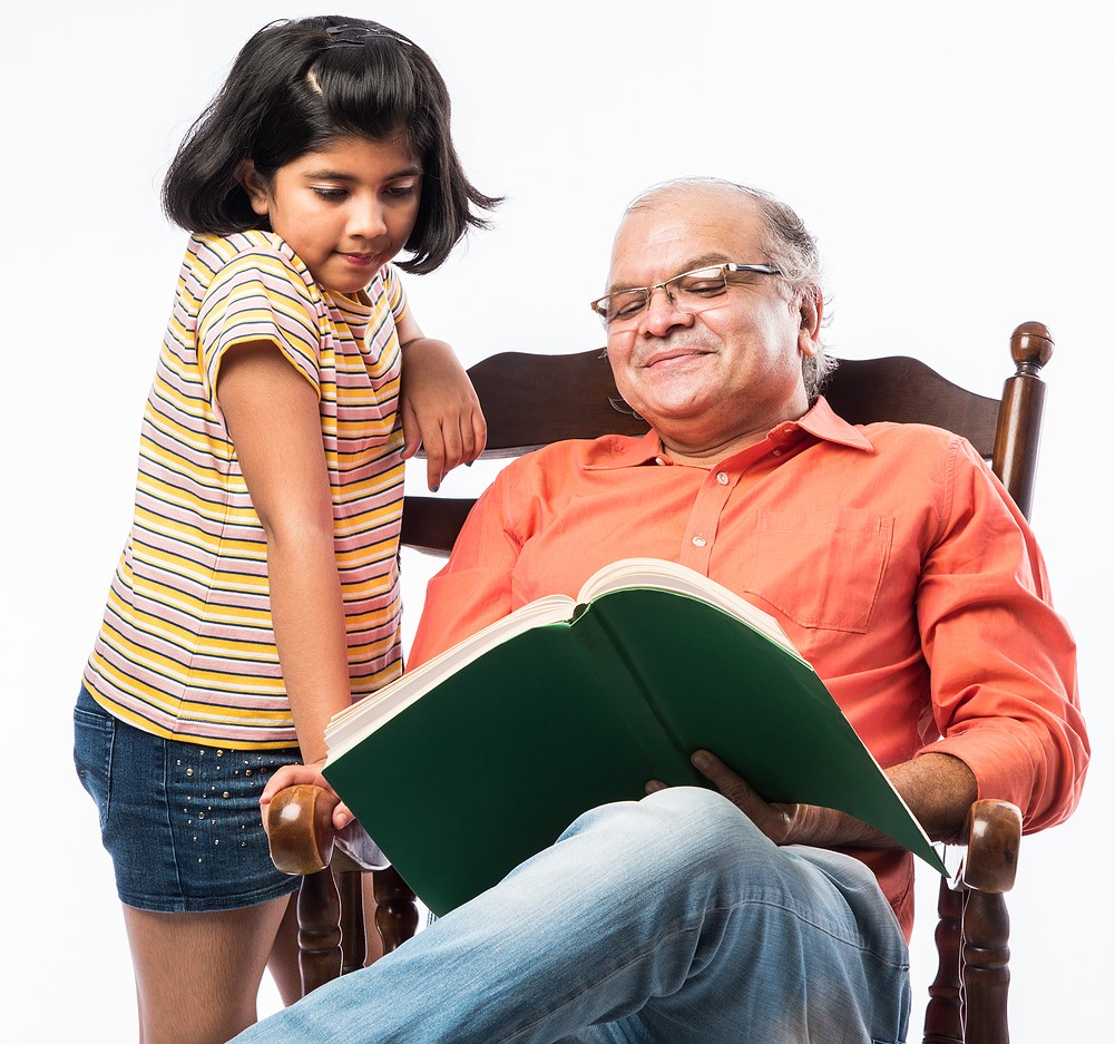 Indian Senior Man Or Grandpa Reading Book With Granddaughter Or